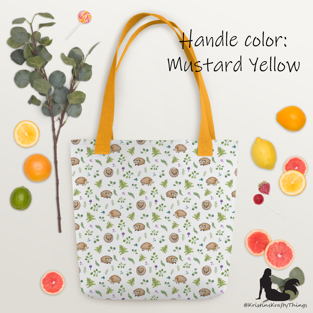 All-over full color print from original watercolor painting. These adorable woodland hedgehogs dance about with green ferns and purple &amp; teal mushrooms on this spacious tote bag to help you carry around everything that matters. Photo of tote bag with black handle on holiday layout.