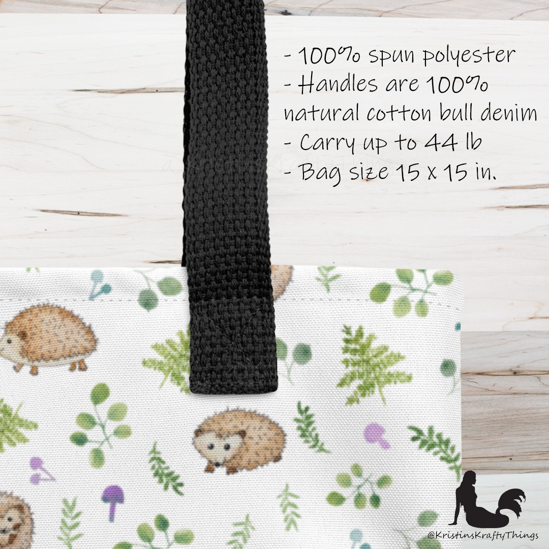 All-over full color print from original watercolor painting. These adorable woodland hedgehogs dance about with green ferns and purple &amp; teal mushrooms on this spacious tote bag to help you carry around everything that matters. Photo of closeup of tote bag with black handle with details about the bag.